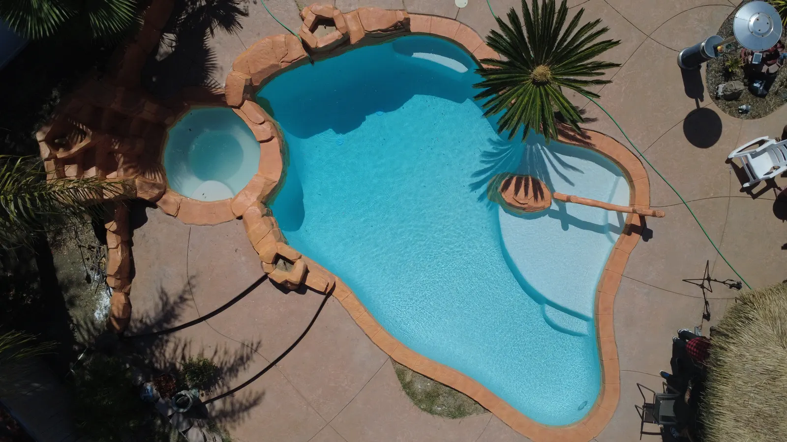 Aerial view of a finished freeform pool with rock waterfall and attached spa, filled with clear turquoise water